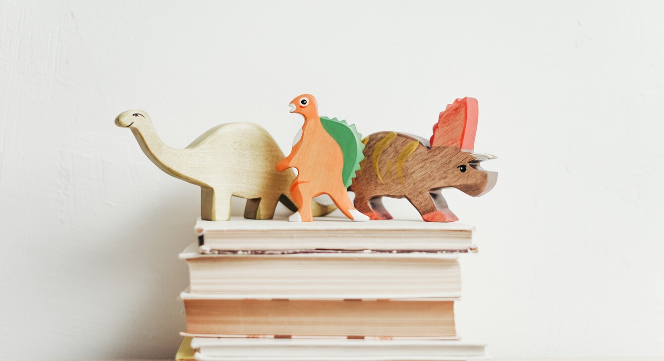 trois dinosaures en bois sur une pile de livres
