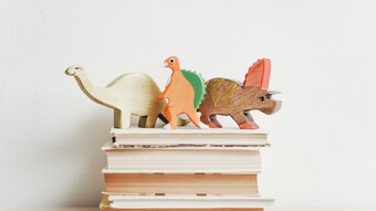 trois dinosaures en bois sur une pile de livres